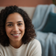 Portrait of a happy person in their 30s, smiling warmly, with a blurred background in dusty blue and deep teal.